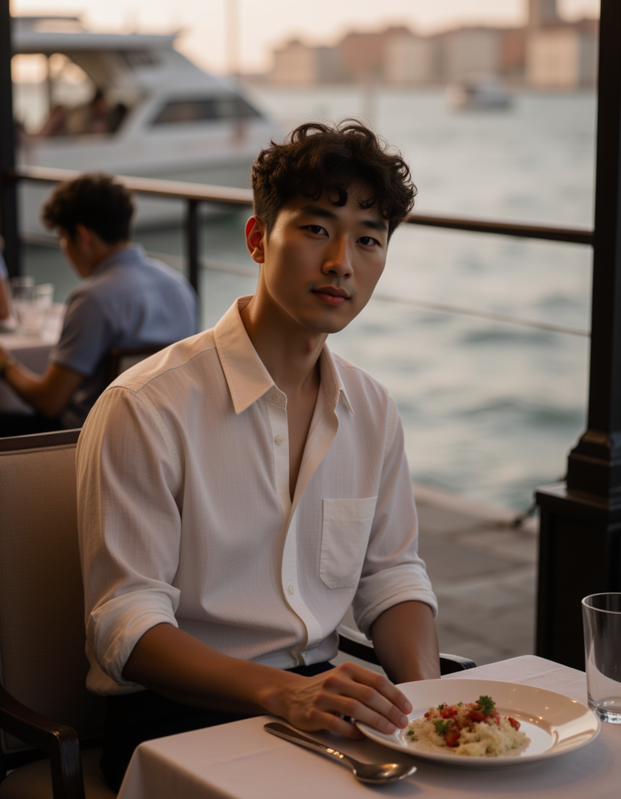 a charismatic figure seated at a waterfront table in Little Venice during blue hour, waves crashing gently nearby, warm glow from the taverna lighting his face as he looks directly at the camera, wearing a tailored linen shirt, high-end travel photography style